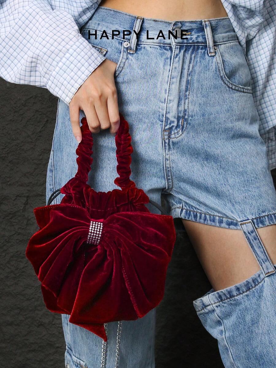 HAPPY LANE Feita de veludo vermelho encantador com um toque suave, esta bolsa apresenta um laço grande e glamoroso adornado com strass brilhantes, misturando luxo e elegância divertida. Ela vem com uma alça franzida e alça de ombro de corrente de metal, oferecendo versatilidade para estilos de transporte à mão ou a tiracolo. Perfeita para eventos noturnos, festas ou ocasiões especiais, esta peça adiciona um charme refinado e gracioso ao seu conjunto