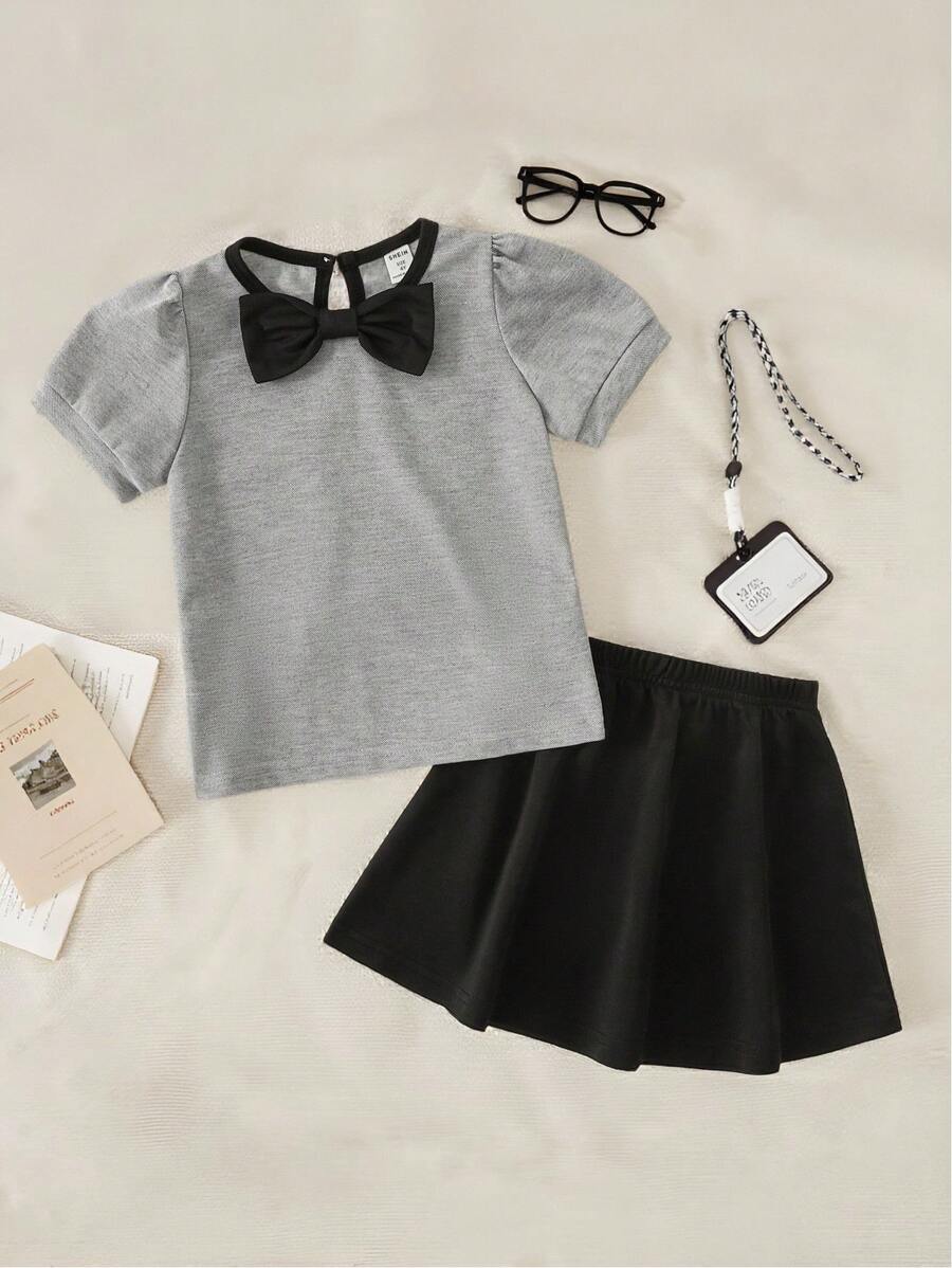 Maglietta girocollo per ragazze con fiocco, in stile semplice e femminile da college, abbinata a una gonna corta. Outfit da college e abbigliamento sportivo per il ritorno a scuola della stagione 2025
