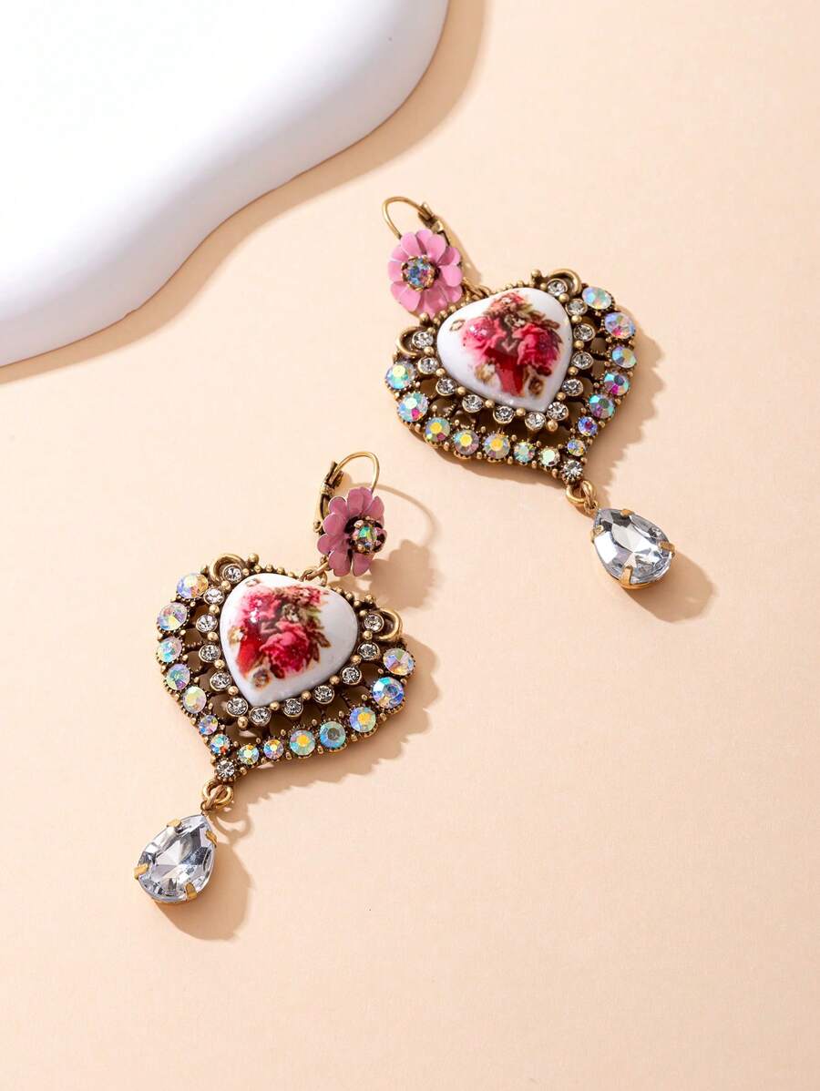 Il s'agit d'une paire de boucles d'oreilles bien conçues. Le style appartient à l'esthétique vintage et romantique, en mélangeant divers éléments : - Conception principale : Pièces en céramique en forme de cœur avec des motifs floraux rouges, ce qui donne une ambiance artistique et romantique. - Éléments décoratifs : les bords des formes de cœur sont garnis de nombreux strass scintillants, ajoutant une touche de luxe.