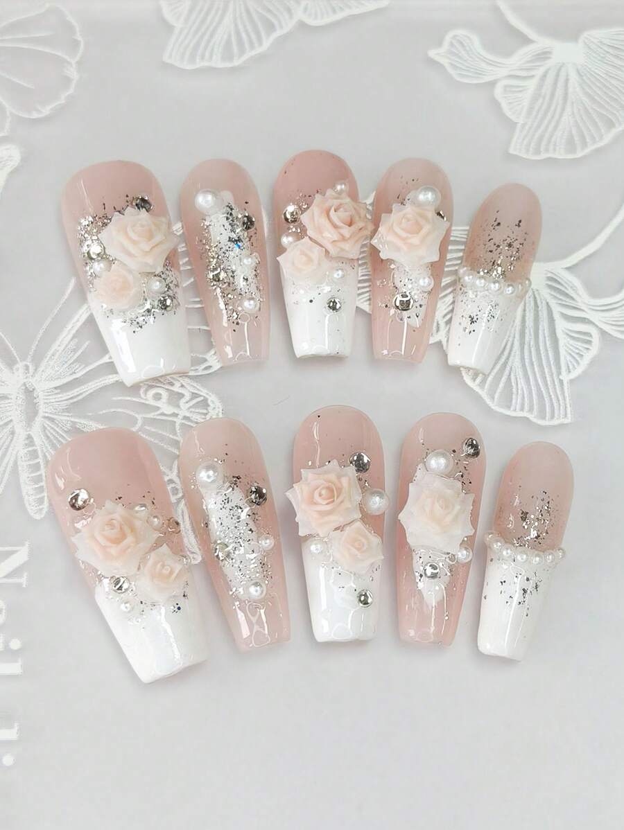 Un ensemble de 10 manucures en forme de cercueil longues et délicatement conçues, avec des pointes françaises blanches peintes à la main style Y2K, des feuilles d'argent et d'or brillantes, ainsi qu'un design 3D haut de gamme avec fleurs de camélia, strass et chaîne de perles de fantaisie.