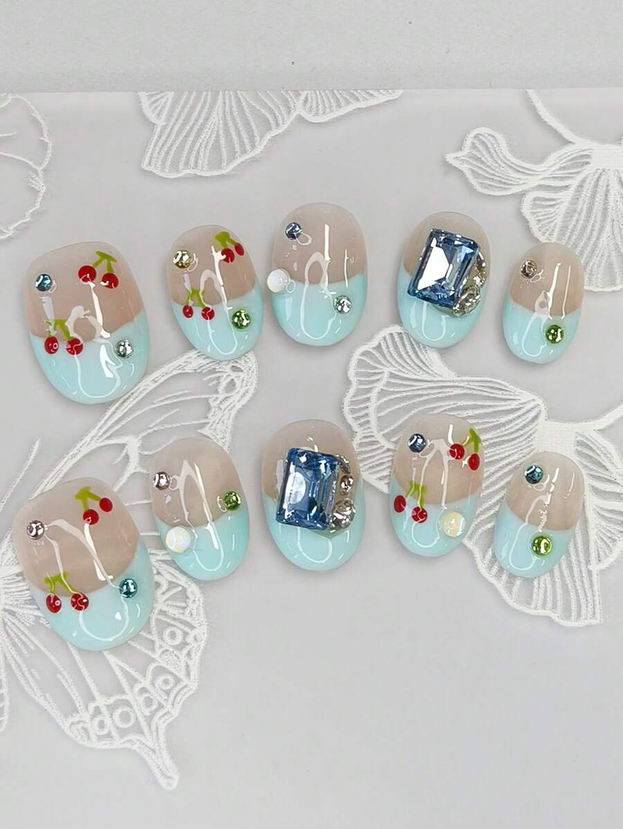 Coffret nail art comprend 10 ongles courts en amande faits main, avec un style French manucure bleu, des cerises peintes à la main et des strass carrés bleus, le tout pour un éclat brillant. Fabriqués selon le nouveau style Ballet Nail.