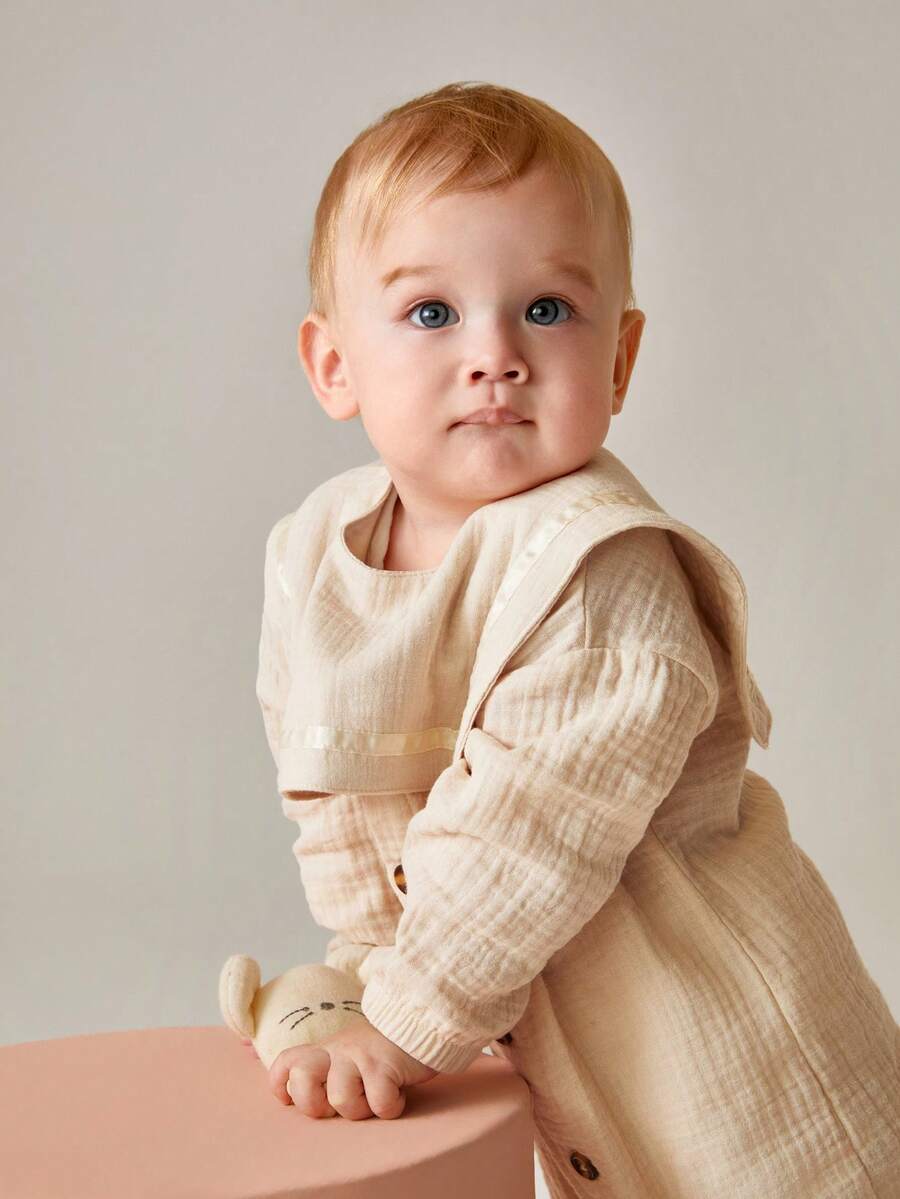 SHEIN 这款男婴杏色褶皱棉质连体衣,配有可拆卸围兜,采用优质面料和精心设计,穿着舒适、方便又时尚。一体式连体衣设计确保保暖,方便更换尿布;可拆卸围兜则让清洁和护理更加便捷。这款连体衣套装让宝宝时刻展现可爱活泼的一面,同时也让妈妈的护理工作更加轻松高效。 - 杏色 - 查看 1