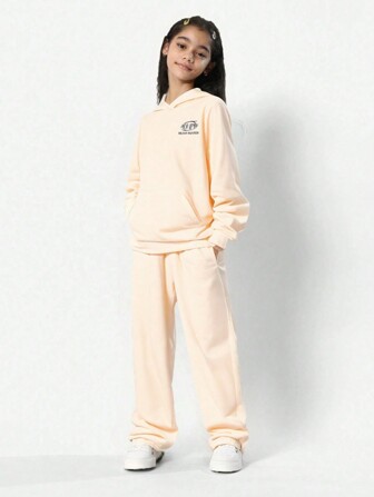 适合 Z 世代女孩的礼物杏色印花连帽长袖上衣和运动裤套装。这套服装由针织运动衫面料制成，正面印有小英文文字，背面印有大英文文字。设计采用兜帽、罗纹袖口和下摆。裤子有松紧脚踝，适合户外活动。