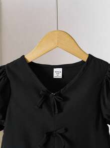 Blusa para niña con cuello en V, mangas abullonadas, volantes en el bajo y decoración de moño