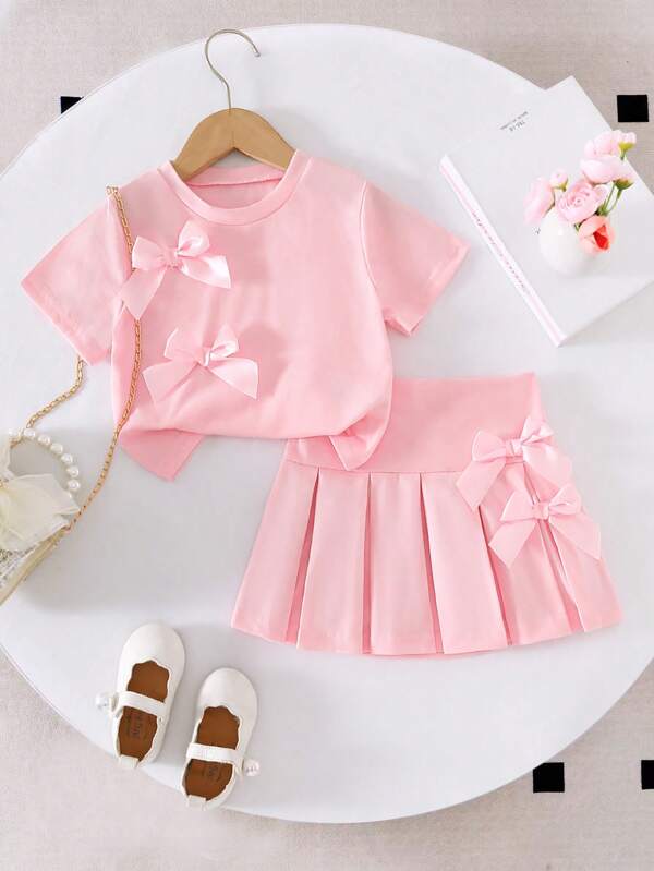 Set de 2 piezas compuesto por una camiseta corta de manga corta con cuello redondo y decoración de lazo en unicolor rosa, y una mini falda plisada de cintura elástica rosa, un conjunto informal y dulce para niñas