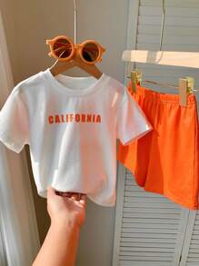 SHEIN Set de 2 piezas de ropa informal deportiva para niño/niña, estilo urbano con estampado de letras, que incluye una camiseta holgada de punto de cuello redondo y unos pantalones cortos de cintura elástica, apta para usar en primavera/verano tanto en casa como al aire libre