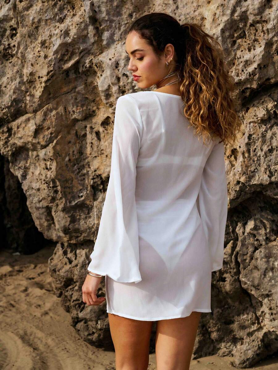 Nöista Durchsichtiges Langarm-Überwurfkleid, zart und leicht, ideal zum Überziehen, mit langen Ärmeln und schmeichelhaftem tiefen Ausschnitt mit verstellbaren Bindebändern für zusätzlichen Charme. Die dezenten Seitenschlitze und die Mini-Länge verleihen einen luftigen, mühelosen Look, der perfekt für Strandspaziergänge oder lässige Sommerstimmung ist.