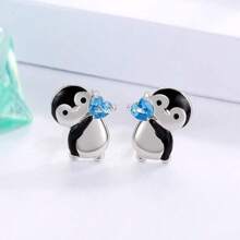 可愛的企鵝拿著藍色心形耳釘,送給女人和女孩的生日和聖誕節禮物