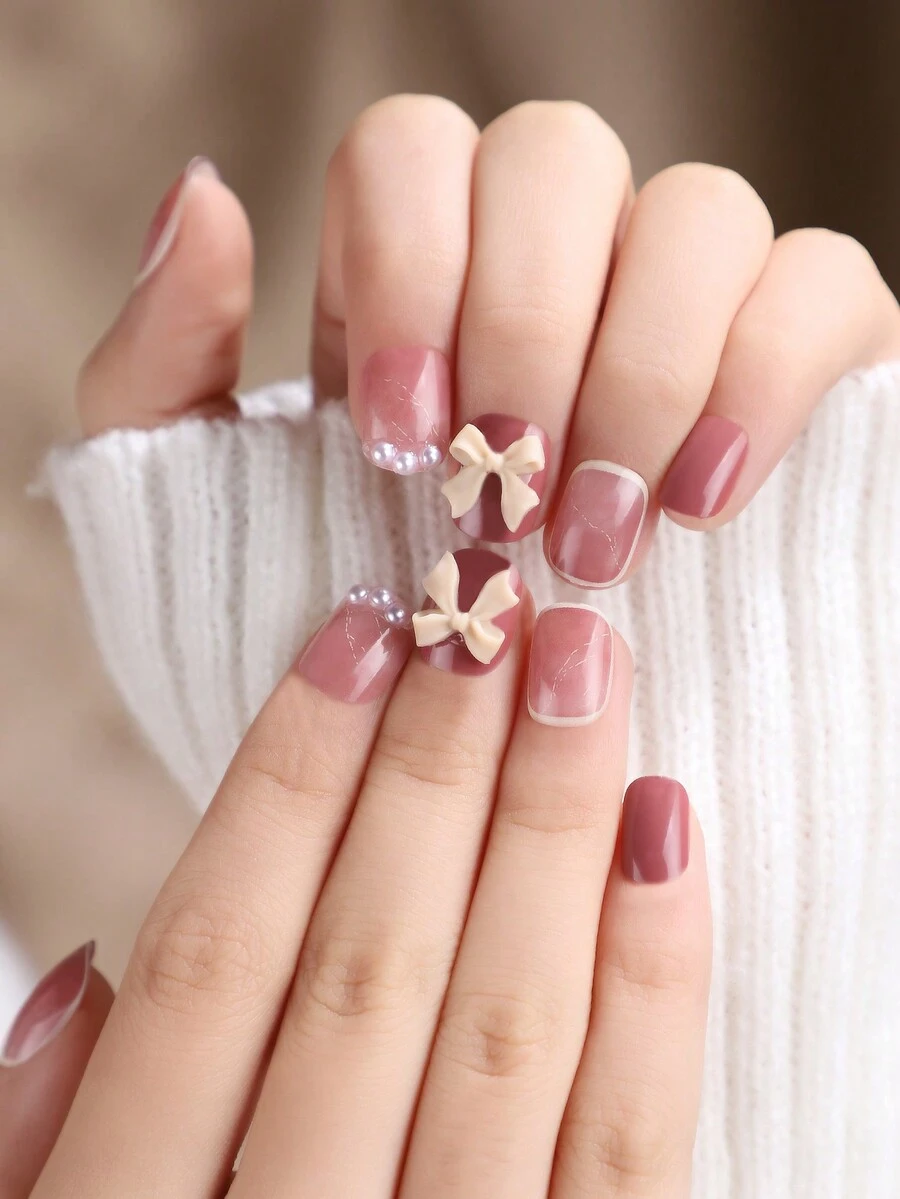 24 móng tay nhân tạo hình vuông ngắn với màu hồng mềm mại dễ thương và trang trí bằng ngọc trai & nơ, bao gồm 1 dũa móng tay và 1 keo thạch trong suốt