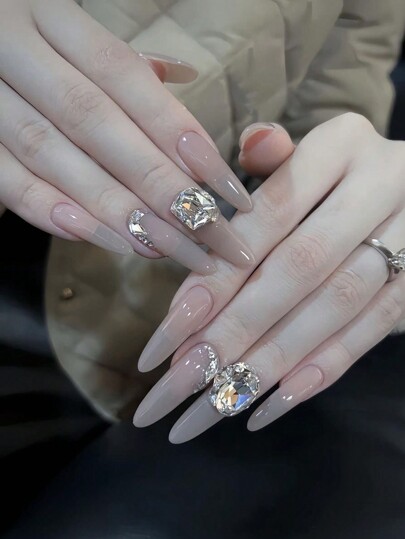 見た目を一瞬でアップグレード！シンプルなヌードカラーと輝くダイヤモンドデコレーションが美しいアーモンド型の假爪が30本入ったフルセット。ジェリージェル1つとネイルファイル1つが含まれます。パーティーやダンス、日常着用に適しており、繰り返し使えます。