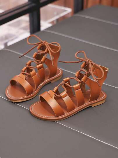 Un par de zapatos romanos planos con tira cruzada, de suela blanda y antideslizantes, de moda y versátiles, apropiados para el verano, para niñas pequeñas