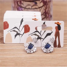 Paquete de 100 piezas de pendientes de gota con diseño de chica guiñando o chica tomando una foto, de 5,5 x 3,5 cm, con tarjeta de embalaje con diseño de patrones