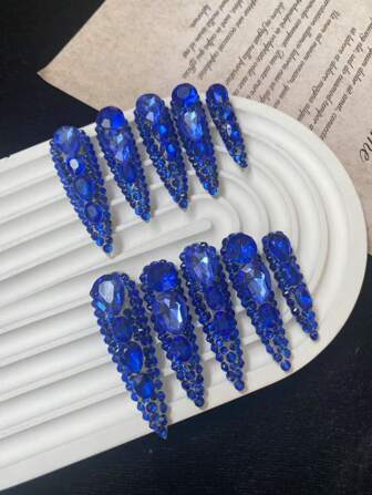 These Ten Hand - Crafted Press - On Nails Are Displayed On A White, Wavy Platform, With A Piece Of Paper With Printed Text In The Background, Creating A Contrast Between The Vivid Nails And The Simple Backdrop. The Nails Are A Bold, Deep Blue Color Nail Supplies Nails