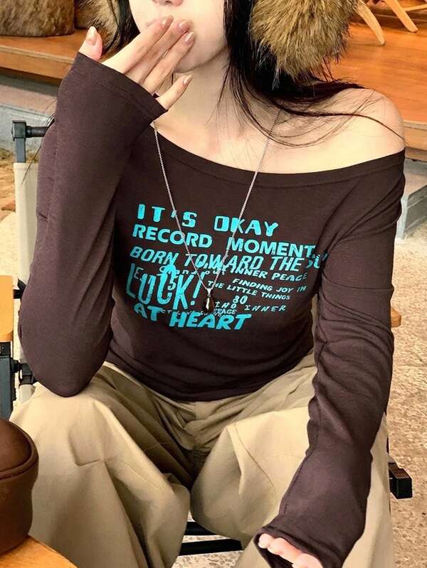 Dazy Plus Áo thun nữ tay dài casual màu nâu in chữ, cổ lệch vai bất đối xứng, phong cách graphic tee cho mùa xuân/thu