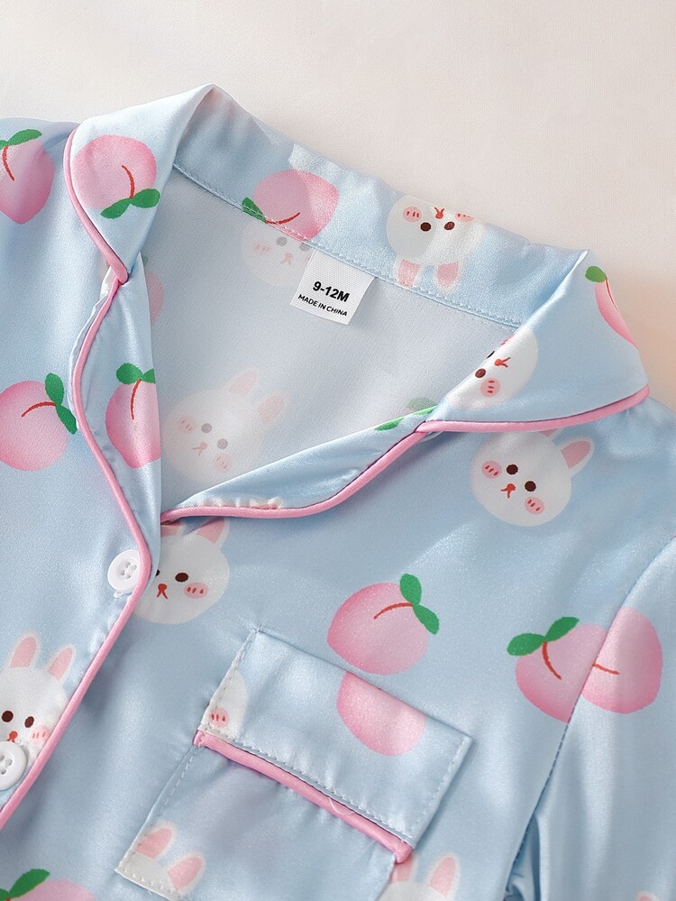 SHEIN Bộ đồ ngủ 2 món ngọt ngào, tươi mát cho bé gái gồm áo cardigan tay ngắn cổ ve lật và quần short cùng màu, được làm từ chất liệu mềm mại, mịn màng như satin. Bộ đồ mặc nhà mùa hè thoải mái này có họa tiết thỏ hoạt hình và quả đào màu hồng nhạt điểm xuyết sắc xanh dễ thương, tạo nên vẻ ngoài thời trang cho bộ đồ ngủ thường ngày của bé gái. - Màu xanh lam - Xem 7