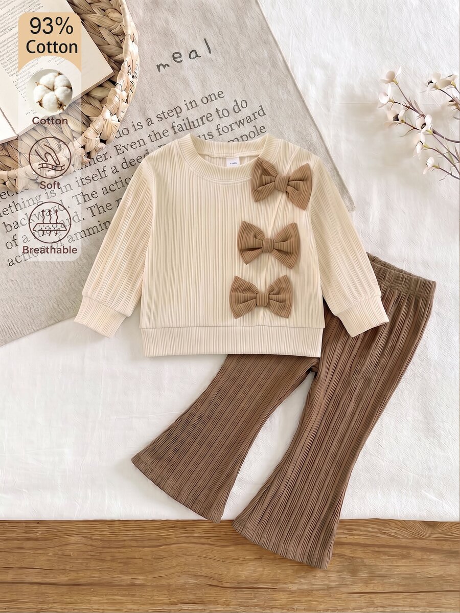 SHEIN طقم ملابس أنيق من قطعتين للبنات الصغيرات، ملابس علوية بأكمام طويلة بلون مشمشي فاتح مع خطوط مضلعة وتصميم غير متماثل مزينة بفيونكة بألوان متباينة، وبنطلون طويل بني واسع، مناسب للخريف والشتاء