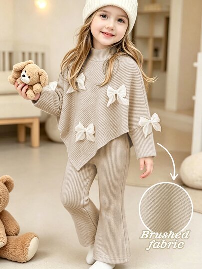 SHEIN Elladie kids (فتاة صغيرة) طقم تي شيرت كاجوال للخريف/الشتاء، تصميم مستوحى من غير متماثل بياقة عالية منسوجة مضلعة من قماش ناعم بلون مشمش فاتح مع ديكور فيونكة بيضاء ثلاثية الأبعاد على الصدر، تي شيرت بأكمام طويلة مقترن ببنطلون طويل واسع بلون مشمش فاتح موحد، طقم من قطعتين مناسب لموسم العودة إلى المدرسة في الخريف/الشتاء، ملابس أنيقة راقية للاستخدام اليومي والمدرسة والخروجات والسفر والحفلات