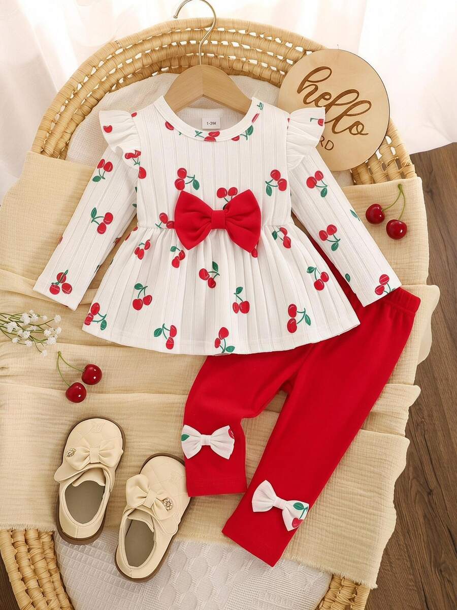 SHEIN 這套 2 件式女嬰套裝走休閒可愛甜美韓風，包含白色長袖修身上衣，飾有蝴蝶結細節與櫻桃印花圓領，搭配純紅色鬆緊腰長褲，適合秋冬日常穿著、公園野餐、遊樂園、度假、拍照及其他室內外活動
