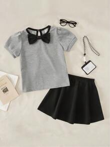 Maglietta girocollo per ragazze con fiocco, in stile semplice e femminile da college, abbinata a una gonna corta. Outfit da college e abbigliamento sportivo per il ritorno a scuola della stagione 2025