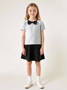 Maglietta girocollo per ragazze con fiocco, in stile semplice e femminile da college, abbinata a una gonna corta. Outfit da college e abbigliamento sportivo per il ritorno a scuola della stagione 2025