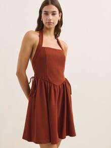 Nöista 这款铁锈色迷你连衣裙采用挂脖式领口，廓形修身喇叭形，侧面饰有精致系带。复古风格的设计和鲜艳的色调，使其成为夏季场合的完美之选，充满俏皮感。