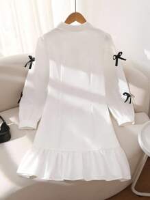 女式白色衬衫裙，学院风泡泡袖，刺绣领口，袖口饰有黑色蝴蝶结。荷叶边下摆设计增添甜美优雅气息，适合休闲、约会等场合，春秋冬皆宜