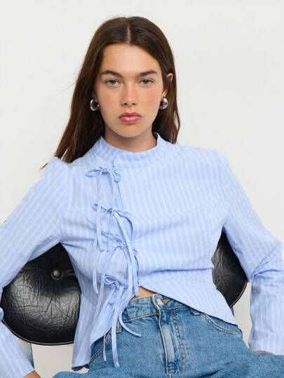 Nöista 这款蓝白条纹衬衫搭配蝴蝶结细节，散发着浓郁的复古学院风。无论是秋季女装、返校季，还是商务休闲风，它都是理想之选。可爱的长袖和独特的设计，使其成为秋冬叠穿的亮点。