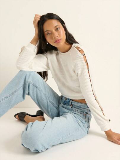 Nöista 白色针织长袖上衣搭配牛仔裤，是秋季百搭单品，非常适合休闲购物。袖口独特的金属扣设计增添时尚感，并形成别致的镂空结构。春秋微凉时节可单穿，也可叠穿打造休闲街头风。