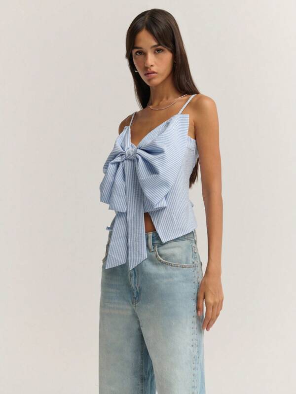 Nöista 上衣的设计亮点在于胸前超大立体蝴蝶结装饰，极具视觉冲击力，少女感十足。面料为浅色棉质，蓝白细条纹，风格甜美休闲。可搭配牛仔短裤或牛仔裤，展现清爽甜美的气质。无论是度假、旅行还是海边，都适合穿着，打造活力时尚的形象。