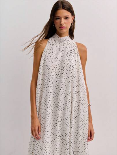 Nöista 这款带有黑色圆点的白色无袖连衣裙采用高领口、长领带、流畅的不对称轮廓和侧开衩设计，将复古优雅与 Y2K 和秋冬季街头风格融为一体。