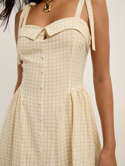 Nöista 这款奶油色迷你连衣裙展现出精致的格纹图案、前扣开合和迷人的喇叭裙廓形。肩部系带装饰和裙摆处的柔和褶皱更增添了一丝魅力。