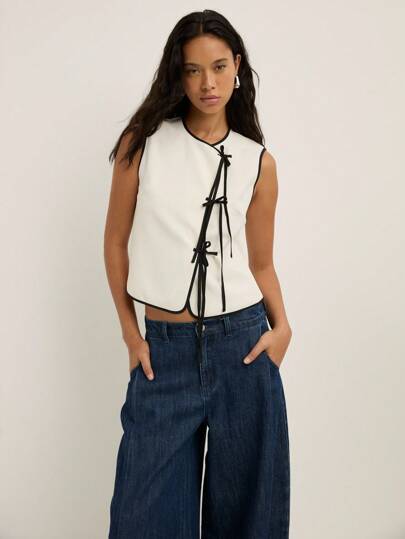  Nöista White Sleeveless Top Trimmed With Black Piping And Adorned With Stylish Black Bow Ties Along The Front, Featuring A Fitted Silhouette Perfect For Fall Women Clothes. Casual, Office, Back To School, Concert, And Boho Autumn Outfits, Winter, Cute, Elegant, Night Out, Halloween.