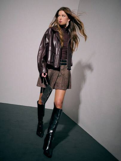 Nöista Falda A-Line de tweed marrón con un cinturón negro ancho y de doble capa con hebillas metálicas; se combina con suéteres ajustados y botas altas para looks retro-modernos de otoño y apariencias elegantes de invierno en los mercados navideños.