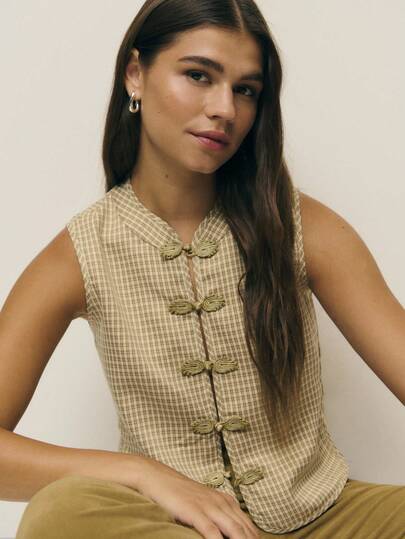 Nöista 这款精致的无袖格纹上衣采用轻盈面料制成，饰有简洁的立领和标志性的前襟青蛙扣。修身却不失宽松的廓形，腰部以微妙的缝线勾勒出优美的线条，透气的梭织面料则赋予其柔和的支撑性和易于叠穿的特性。适合秋冬季节的百搭造型。