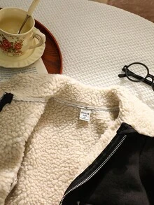 年轻女孩黑色仿麂皮羊毛复合夹克，采用柔软的麂皮羊毛复合纹理，衣领、下摆和袖口处饰有奶油色羊毛饰边，银色拉链开合，对称仿口袋，圆形纽扣装饰，剪裁剪裁融合了复古与时尚风格，秋冬