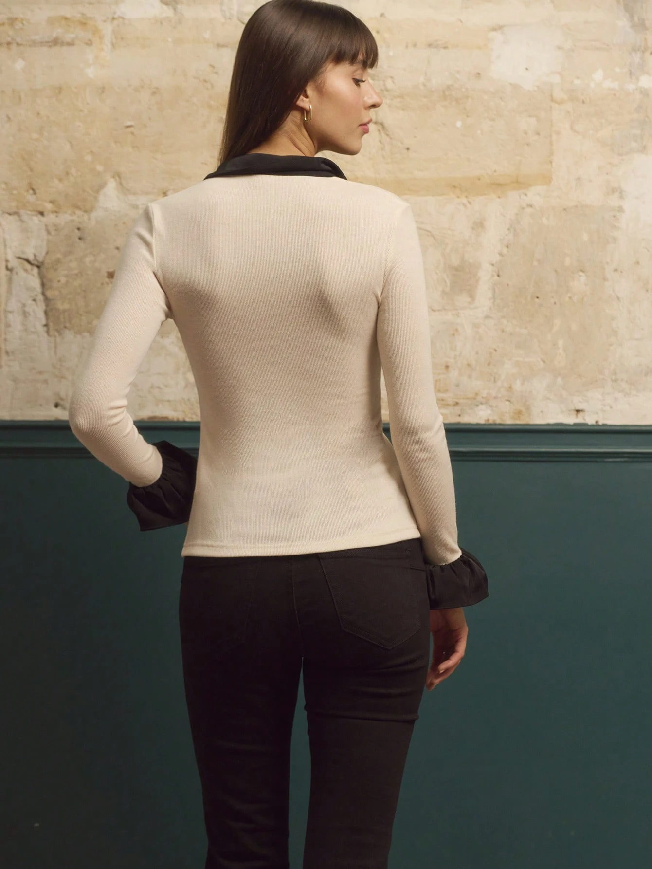 Camicia in maglia beige con volant neri a contrasto e maniche lunghe con polsini a campana, stile vintage chic per l'autunno e l'inverno.