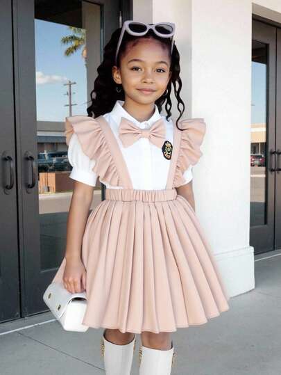 Conjunto de camisa con cuello, manga corta y escudo, y falda plisada con tirantes y mangas con volantes estilo académico en azul marino para niñas