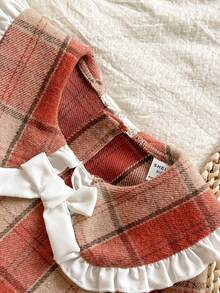 Vintaside Kids Váy len cổ búp bê kẻ caro màu nâu ấm áp, tay dài vừa phải, phong cách sinh viên ngọt ngào và cổ điển này có họa tiết caro đỏ cam và kaki, vừa cổ điển vừa dịu dàng. Được làm từ vải tweed thô, váy có độ dày vừa phải và dáng rộng. Ve áo rộng với viền ren trắng và nơ trắng ba chiều ở giữa, tạo điểm nhấn ấn tượng. Thiết kế khóa kéo phía sau giúp bạn dễ dàng mặc vào và cởi ra. Váy phù hợp để mặc đi học. - Nhiều màu - Xem 4