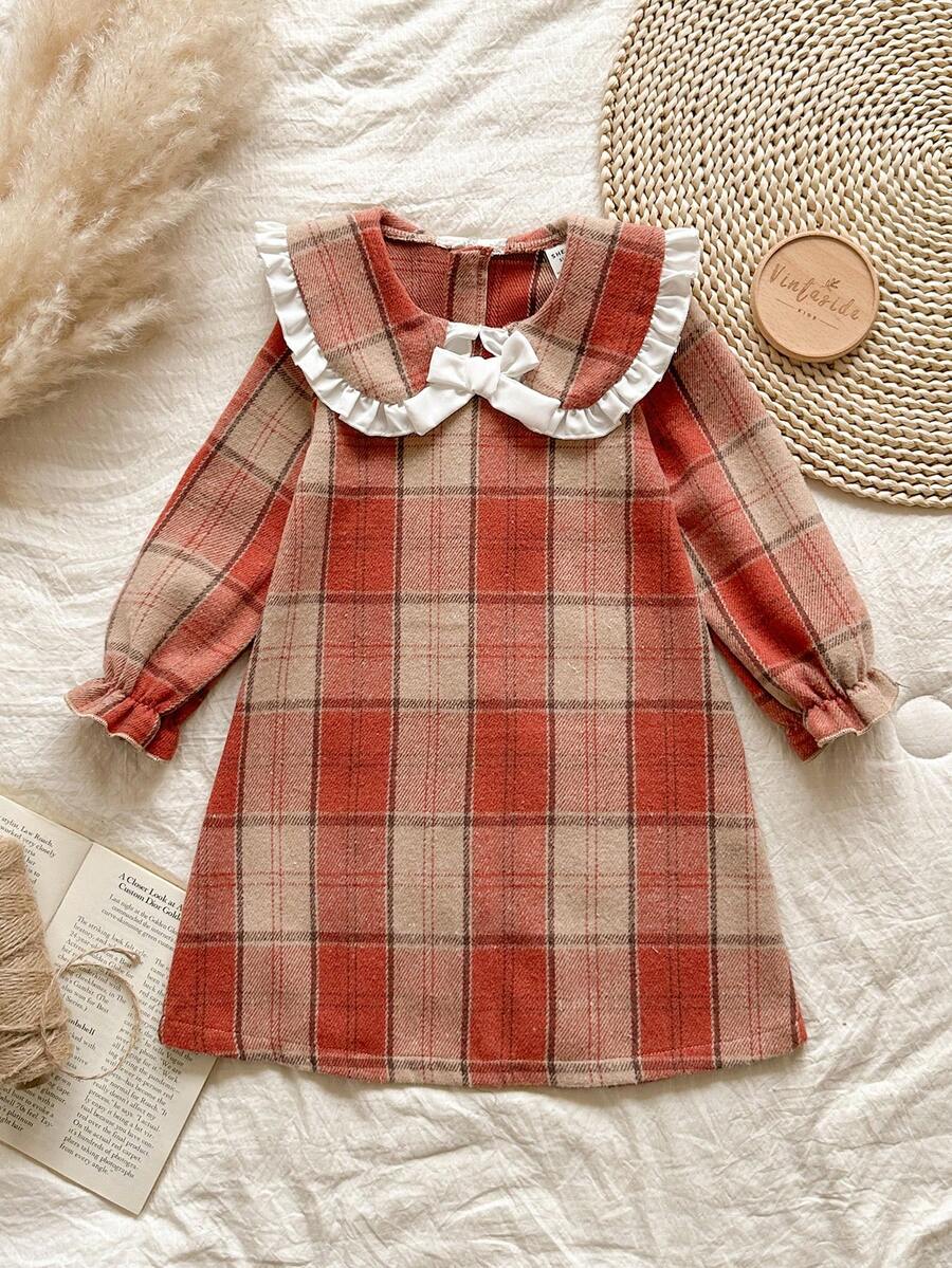 Vintaside Kids Váy len cổ búp bê kẻ caro màu nâu ấm áp, tay dài vừa phải, phong cách sinh viên ngọt ngào và cổ điển này có họa tiết caro đỏ cam và kaki, vừa cổ điển vừa dịu dàng. Được làm từ vải tweed thô, váy có độ dày vừa phải và dáng rộng. Ve áo rộng với viền ren trắng và nơ trắng ba chiều ở giữa, tạo điểm nhấn ấn tượng. Thiết kế khóa kéo phía sau giúp bạn dễ dàng mặc vào và cởi ra. Váy phù hợp để mặc đi học. - Nhiều màu - Xem 1