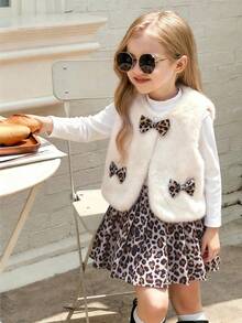 Kleine Mädchen Vintage Chic Outfit bestehend aus cremefarbener Kunstfell Weste, Leoparden Cord Rock und weißem Rollkragenpullover. Die Weste besteht aus weichem Kunstfell mit Leoparden Muster Schleife und Tasche. Der Cord Rock ist komplett mit Leoparden Muster. Dieses modische Retro-Stil Outfit ist geeignet für Wochenendausflüge, Familienrestaurants usw. Die Kombination aus Kunstfell und Cord bietet ausreichend Wärme für die Herbst-/Wintersaison.