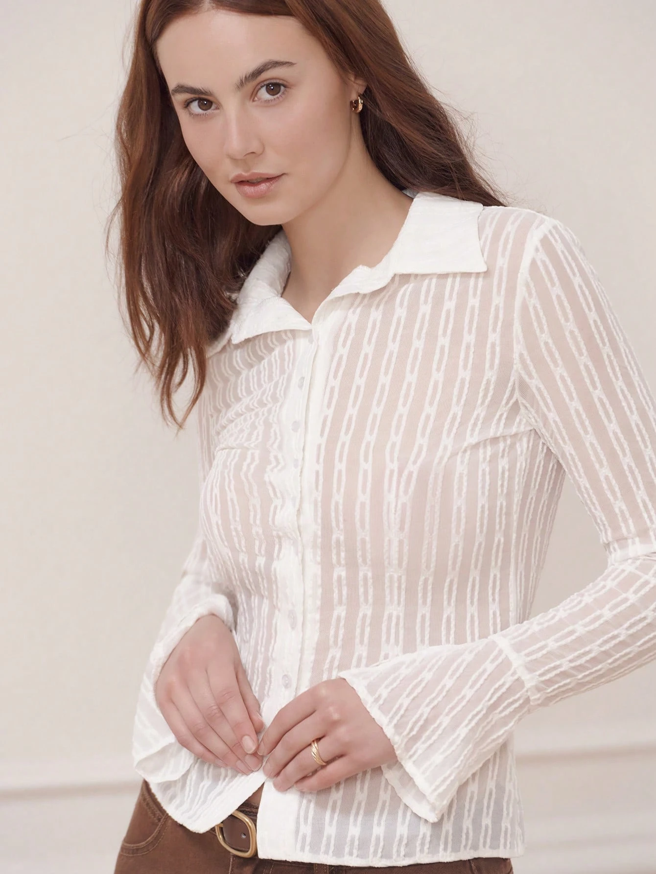 Camisa blanca ajustada y transparente con tela texturizada y puños acampanados