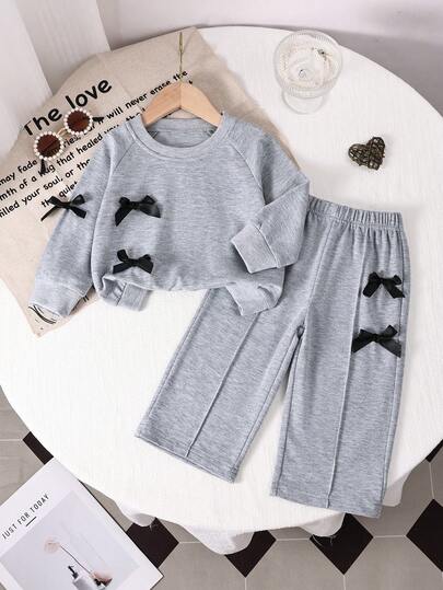 SHEIN 两件套女婴套装，舒适针织圆领长袖卫衣，饰有黑色蝴蝶结，增添可爱风格；搭配灰色松紧腰长裤，同样饰有黑色蝴蝶结，适合户外活动、家庭聚会等各种场合，尤其适合春秋季穿着。