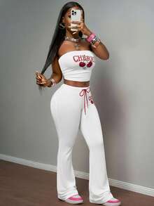 Slaydiva مجموعة بنطلون وكروب توب من قطعتين للنساء، تتكون من: كروب توب أكتاف بارزة ضيق من قماش مضفر وردي مع طباعة حرفية وفواكه كرز، مقترن مع بنطلون ضيق بخصر مطاطي وربطة حبل أحمر بطبعة الكرز، بأسلوب بوهيمي عصري مناسب للحفلات والشاطئ والأعياد، موديل ربيع/صيف 2025