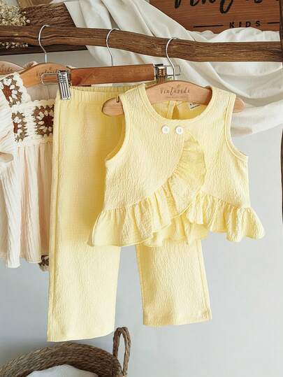 SHEIN Vintaside Kids 这款女童春夏两件套，亮黄色无袖上衣搭配直筒裤，清新甜美又时尚。面料厚度适中，饰有不对称荷叶边和白色纽扣，尽显优雅气质。适合上学通勤、度假旅行、舞蹈练习、居家休闲以及参加派对等各种场合。
