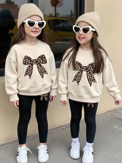 SHEIN Conjunto de 2 piezas para niñas pequeñas, con diseños gráficos de estampados lindos de dibujos animados, estampado de leopardo y decoración de moño, adecuado para otoño, sudadera de cuello redondo en beige + leggings negros, conjunto cálido y cómodo