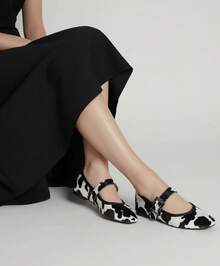 Mary Jane animal print blanco y negro, inspirado en el patrón de vaca; un calzado plano que fusiona vanguardia y actitud lúdica. Su diseño destaca con una correa ancha ajustable adornada con hebilla metálica brillante, corte clásico, punta redondeada y acabado textil de alta calidad que simula pelo natural. Versátil y sorprendente, enriquece atuendos desde los sobrios hasta los creativos. Ideal para quienes buscan originalidad y un toque inesperado en cada paso. - Blanco y Negro - Ver 1