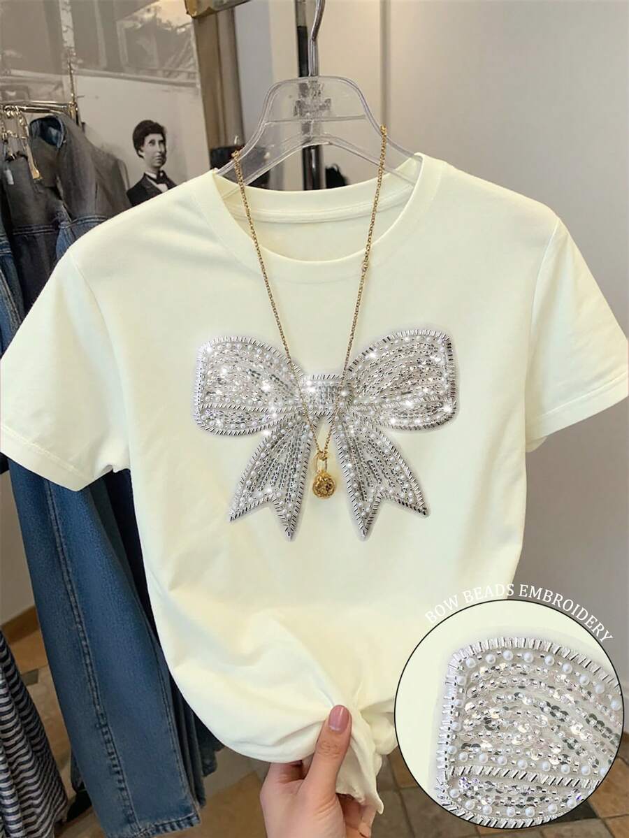 Resyla Áo thun nữ tay ngắn cổ tròn dáng regular fit, thanh lịch với nơ thắt và đính sequin. - Màu be - Xem 1