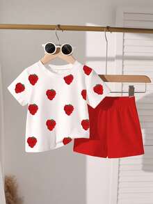 一套甜美可爱的印花圆领短袖T恤和短裤套装，专为女婴设计，适合派对和聚会。T恤采用甜美的草莓印花设计，搭配红色短裤。轻盈舒适，是春夏休闲穿着、户外活动、街头摄影、校园、节日庆典和送礼的理想之选。
