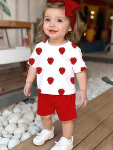 一套甜美可爱的印花圆领短袖T恤和短裤套装，专为女婴设计，适合派对和聚会。T恤采用甜美的草莓印花设计，搭配红色短裤。轻盈舒适，是春夏休闲穿着、户外活动、街头摄影、校园、节日庆典和送礼的理想之选。