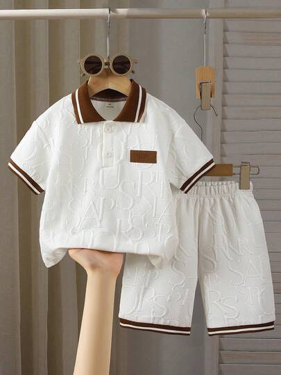 2pcs/Set Toddler Boys' Polo Collar Button-Up Knit Letter Jacquard Polo Shirt & Shorts Set, Sports Casual Style. The Top Is A Short Sleeve Polo Shirt With Brown And White Striped Trim On The Collar And Cuffs, And A Brown Letter Graphic Print On The Body. The Matching Shorts Also Feature The Letter Print And Brown/White Striped Trim, Creating A Coordinated, Well-Designed Outfit Suitable For Children's Daily Wear.